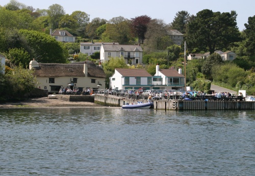 A view of Pandora Inn, in Falmouth, from the sea. The pontoon is busy with pub dwellers and a boat in moored up to the side.